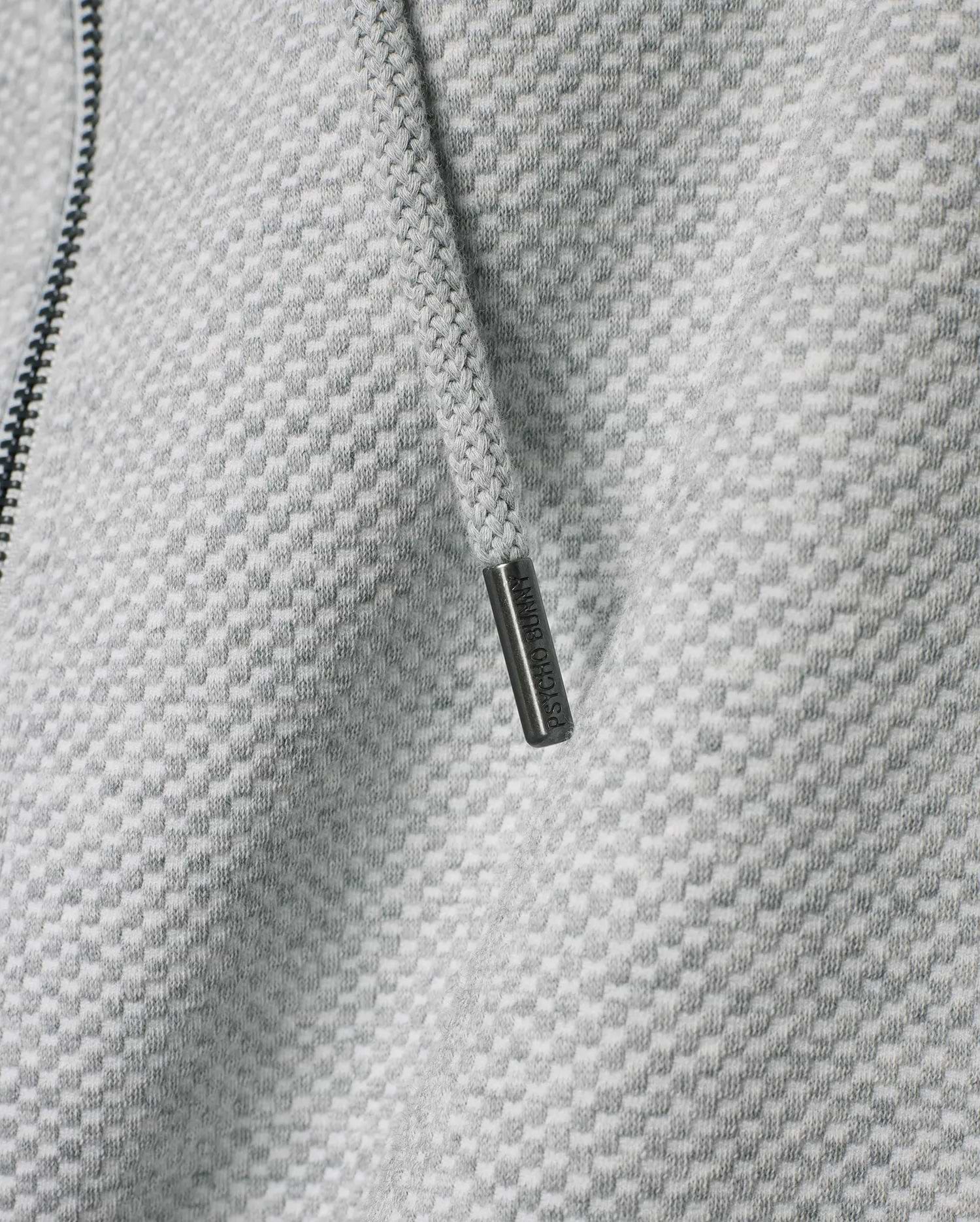 Mens Marc Textured Full Zip Hoodie in light grey with a distinct checkered knit pattern, featuring a dark zipper and a drawstring with an engraved Psycho Bunny metallic tip.