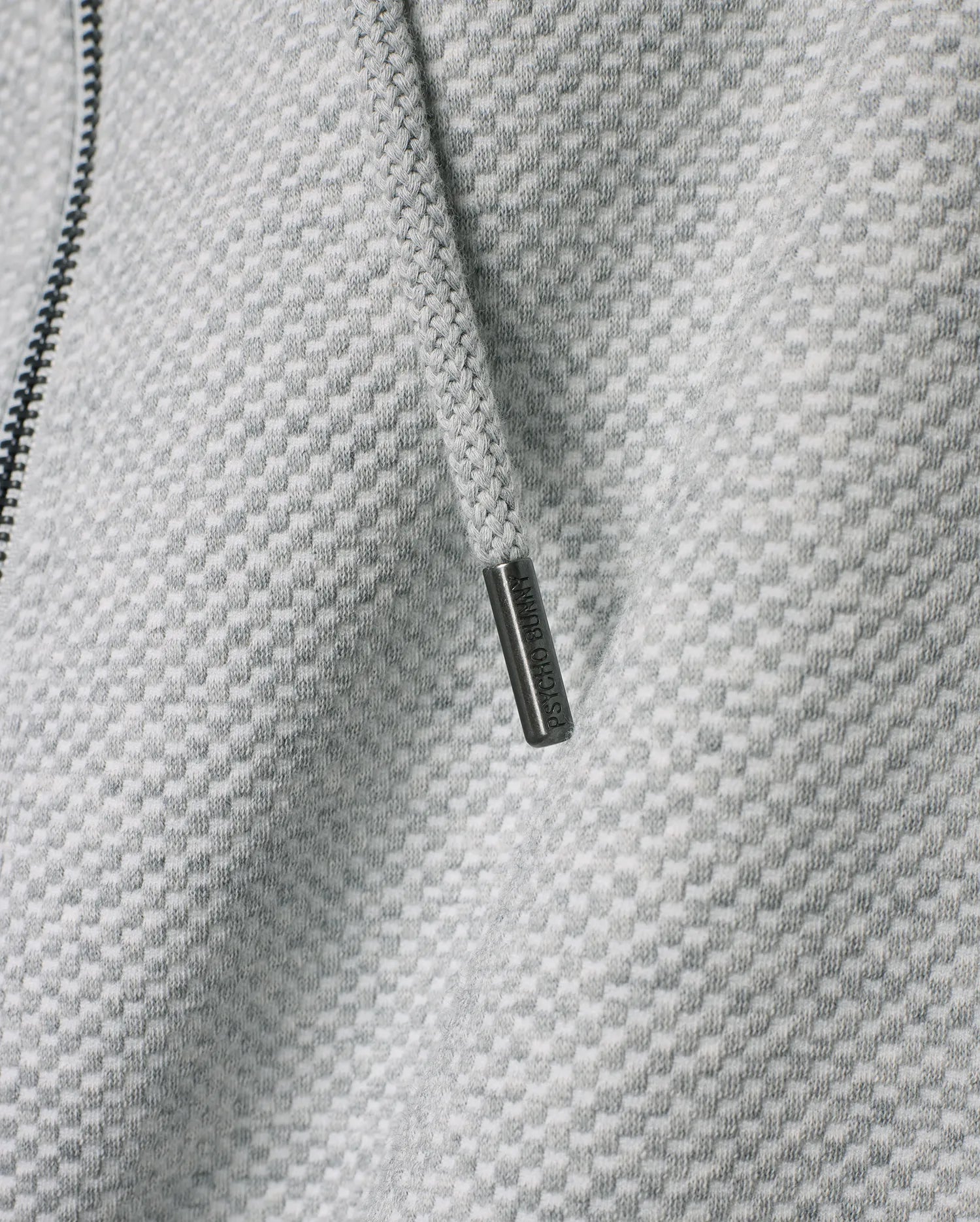 Mens Marc Textured Full Zip Hoodie in light grey with a distinct checkered knit pattern, featuring a dark zipper and a drawstring with an engraved Psycho Bunny metallic tip.