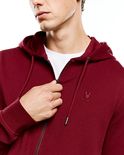 Mens Marc Textured Full Zip Hoodie in deep maroon, featuring a waffle knit texture, full zip closure, drawstring hood with silver tips, and a small embroidered Psycho Bunny skull logo on the left chest.