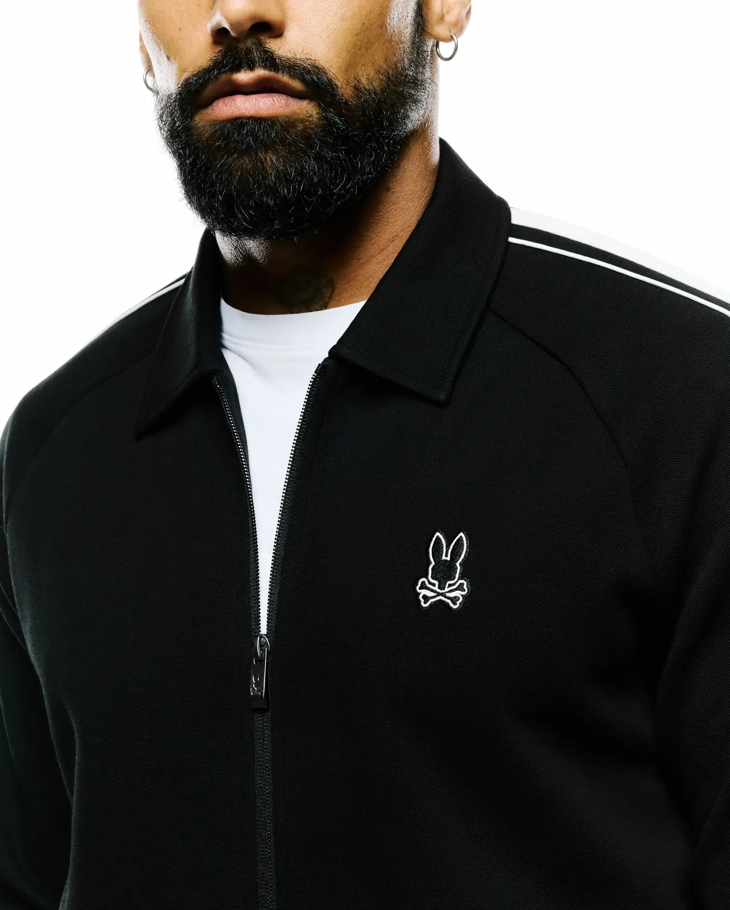 Mens Ceano Track Jacket, black, classic fit, full-zip with a fine knit texture, white shoulder stripes, and a small white embroidered Psycho Bunny skull logo on the left chest.