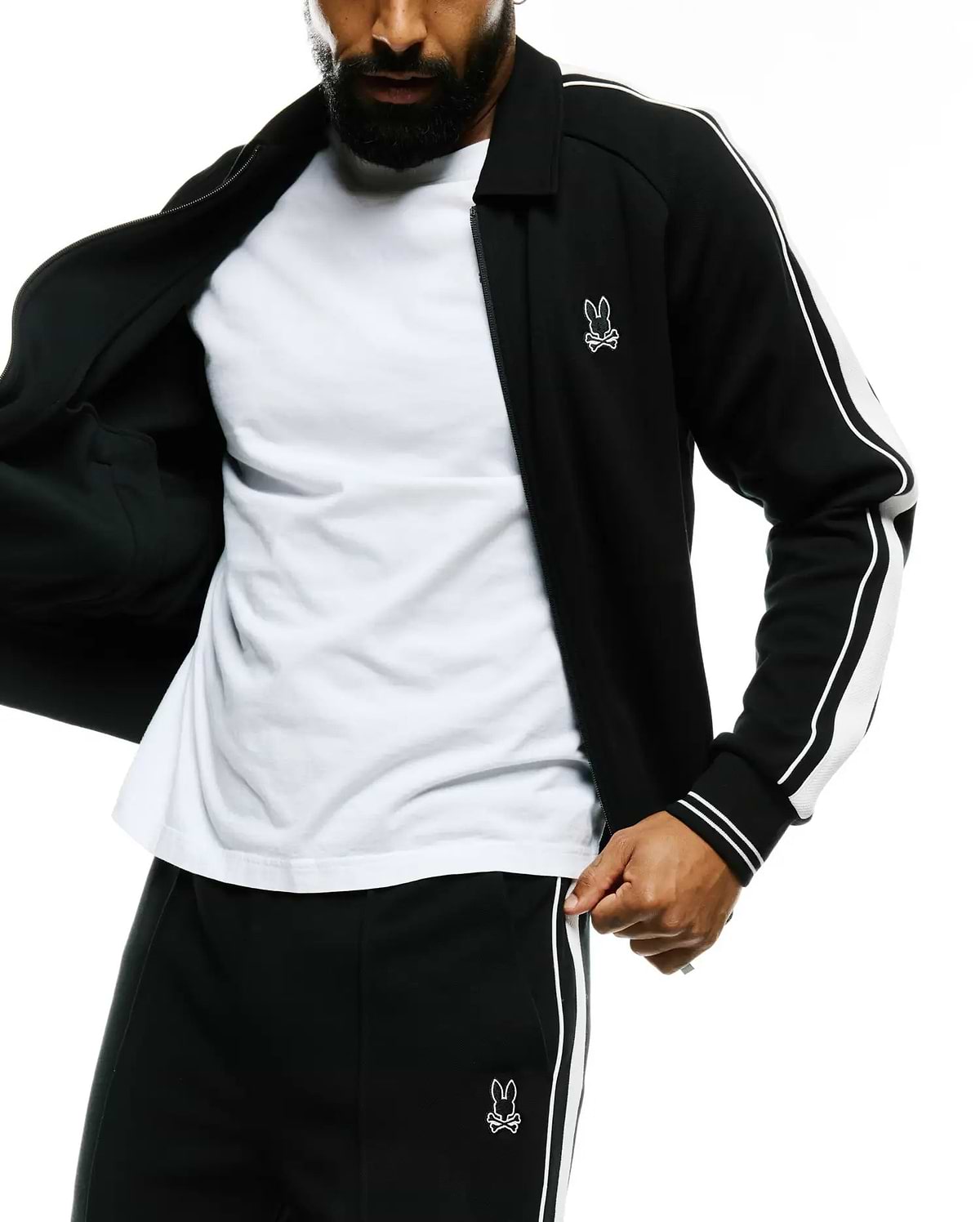 Mens Ceano Track Jacket: Black smooth knit full-zip jacket with classic collar, white double stripes on sleeves, and ribbed cuffs. Features a small white embroidered Psycho Bunny skull logo on the left chest.