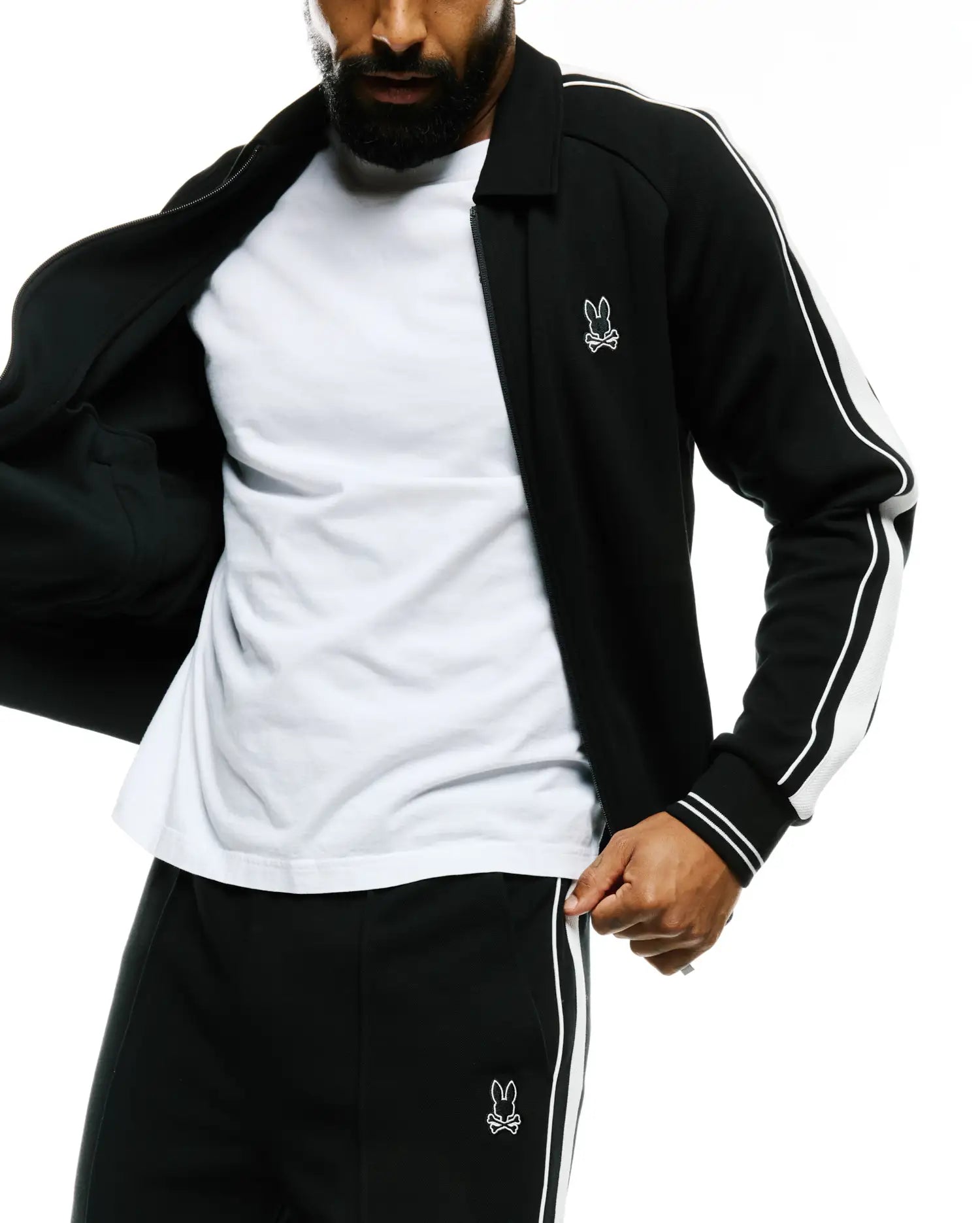Mens Ceano Track Jacket: Black smooth knit full-zip jacket with classic collar, white double stripes on sleeves, and ribbed cuffs. Features a small white embroidered Psycho Bunny skull logo on the left chest.