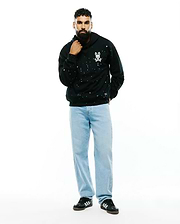 Mens Malcom Splatter Hoodie, a black relaxed fit French terry hoodie featuring an all-over white and teal splatter print and a small embroidered white Psycho Bunny skull logo on the left chest.