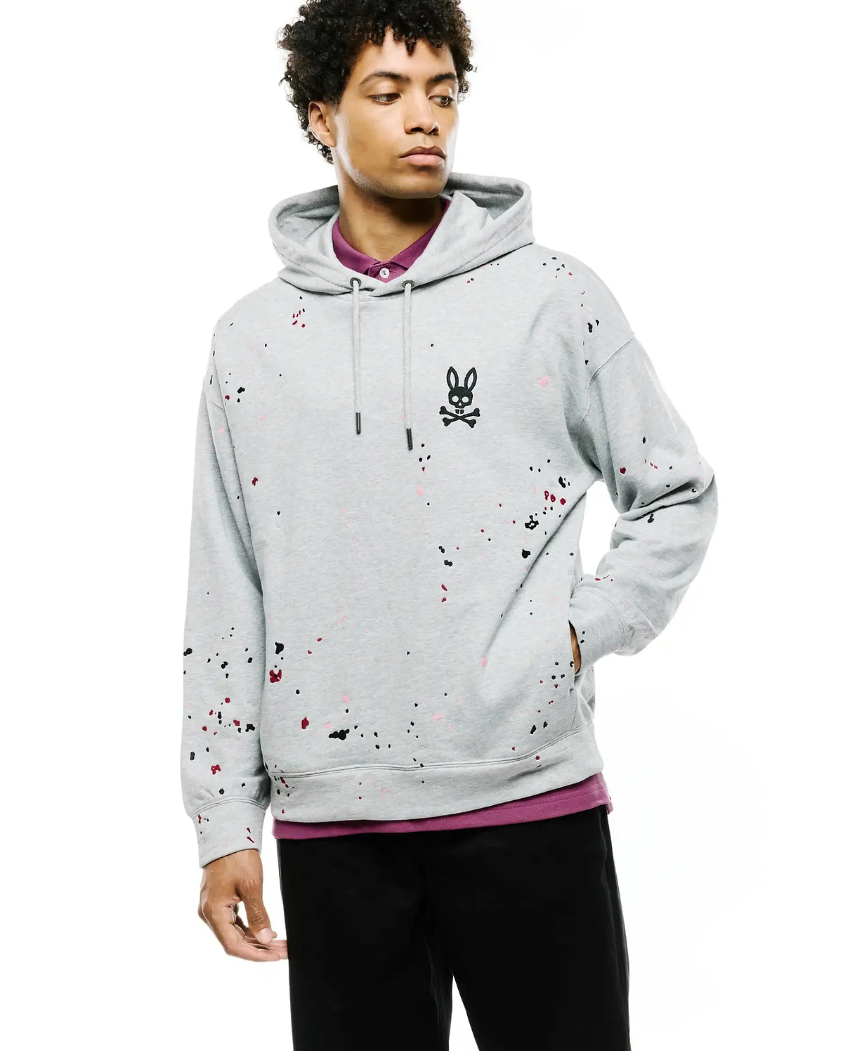 Mens Malcom Splatter Hoodie, a relaxed fit heather grey french terry hoodie featuring a black, red, and pink splatter paint pattern, with an embroidered black Psycho Bunny skull logo on the left chest and a drawstring hood.