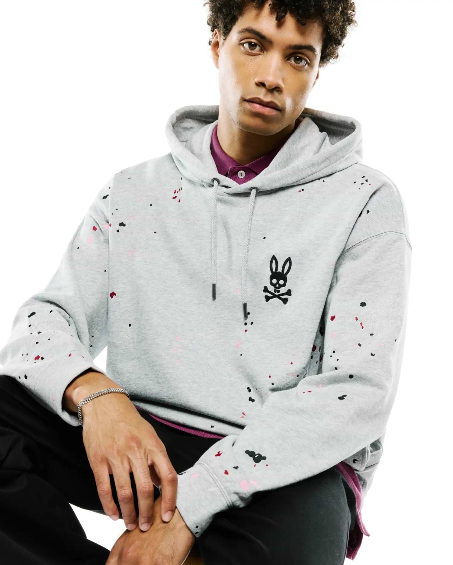Mens Malcom Splatter Hoodie: Relaxed fit heather grey French terry hoodie featuring a vibrant black, pink, and red paint splatter pattern, with an embroidered black Psycho Bunny skull logo on the left chest.