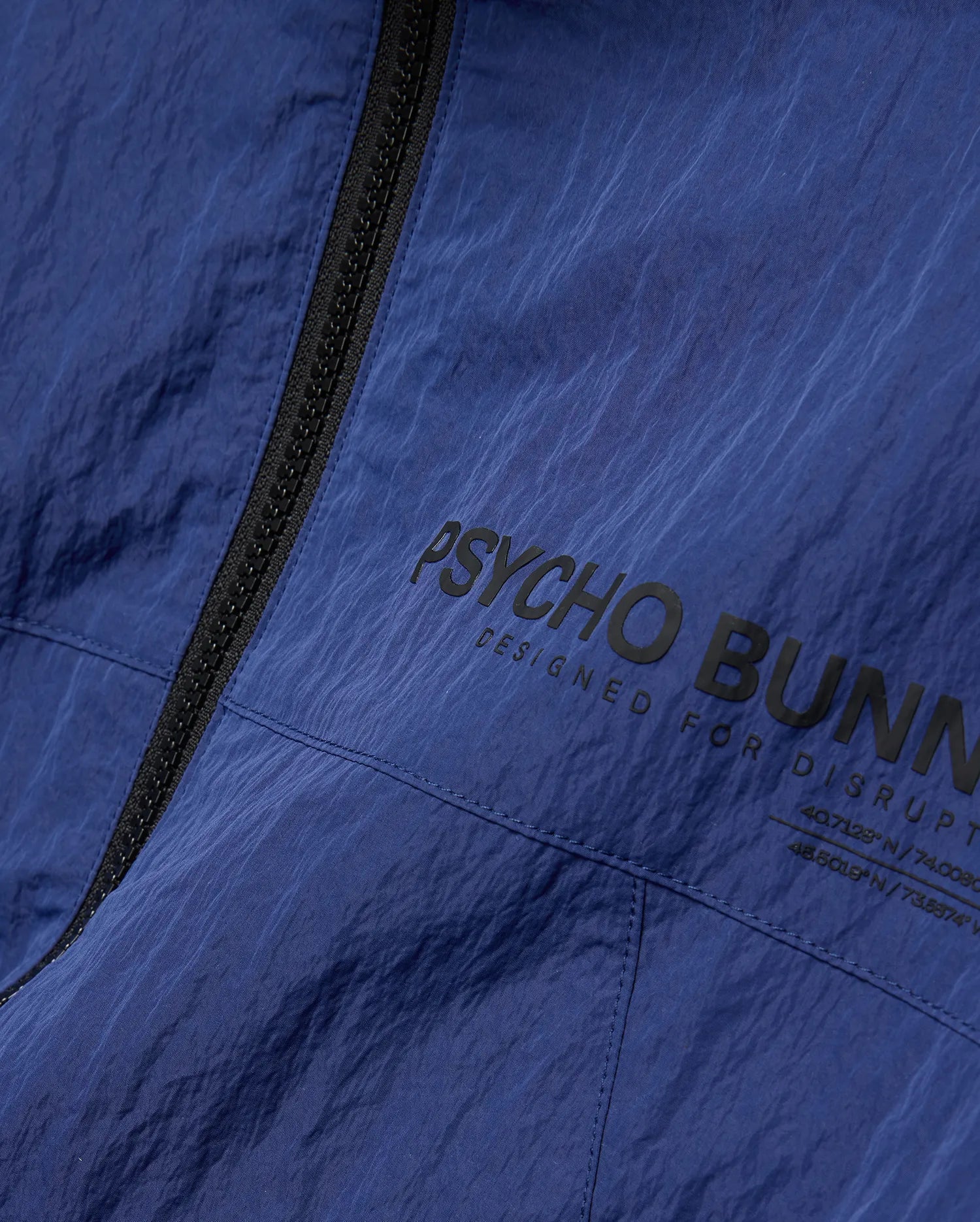 Mens Alder Nylon Jacket in navy blue with crinkled texture, featuring a black full-zip and large black Psycho Bunny text print with Designed For Disrupt slogan and coordinates. (6)