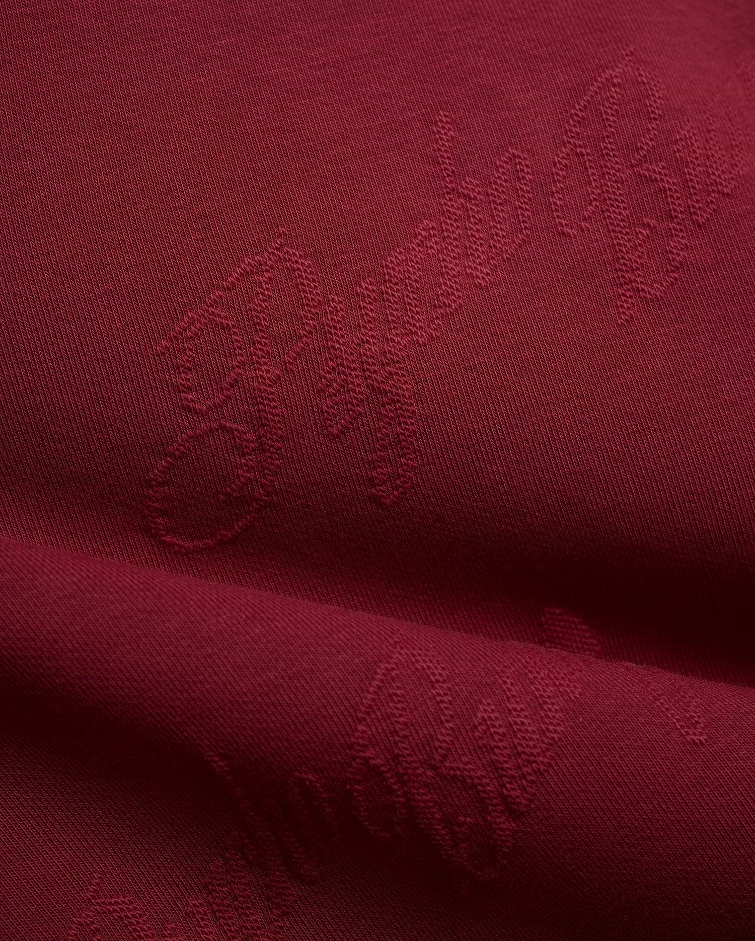 Mens Cedrick All Over Jacquard Crew in deep burgundy, featuring a subtle tone-on-tone jacquard knit pattern of the Psycho Bunny logo and brand name.