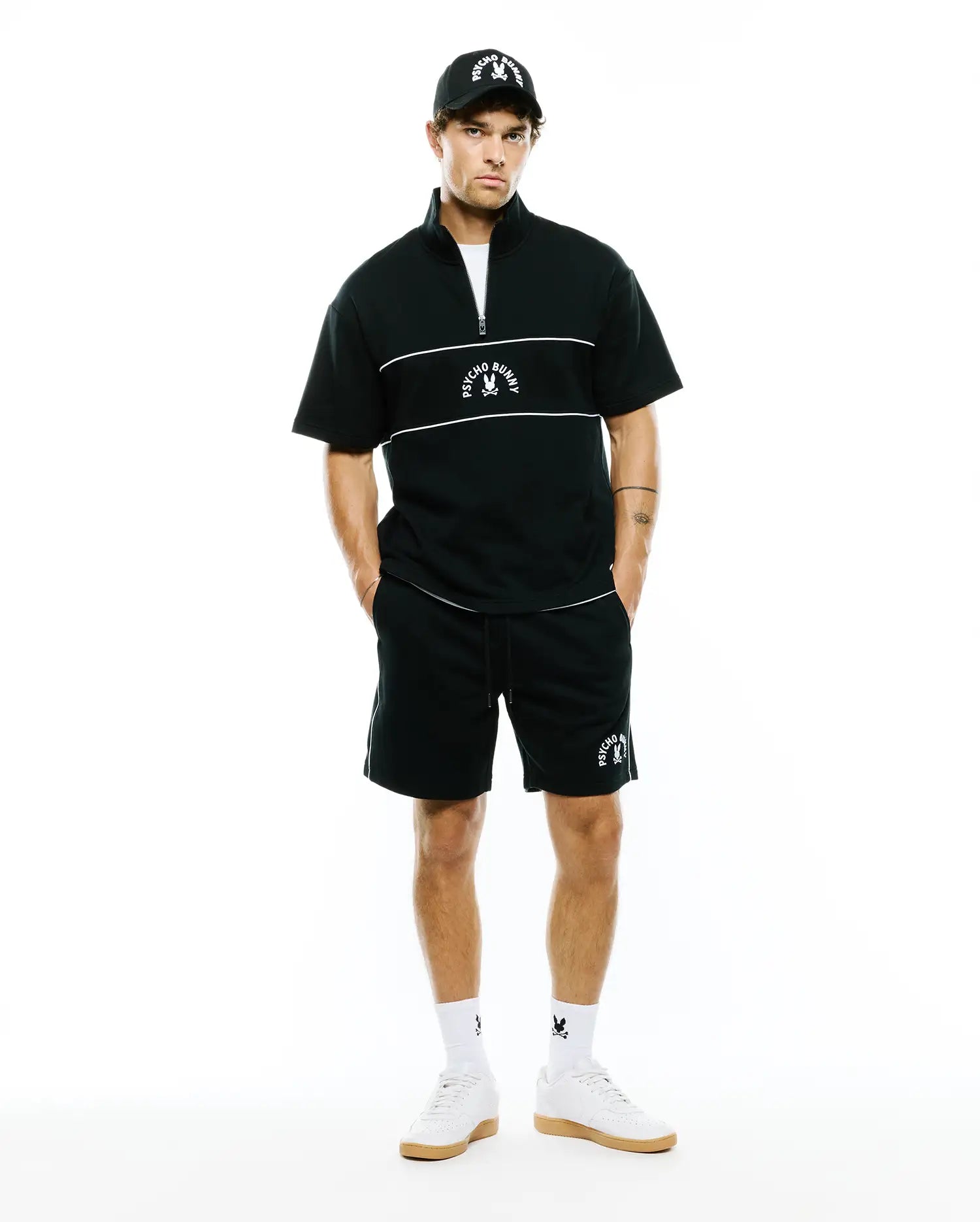Mens Stevie French Terry Ss 1/4 Zip, black relaxed short-sleeve French terry top with white 1/4 zip, chest stripes & embroidered Psycho Bunny logo. Paired with matching black shorts, white piping, bunny skull.