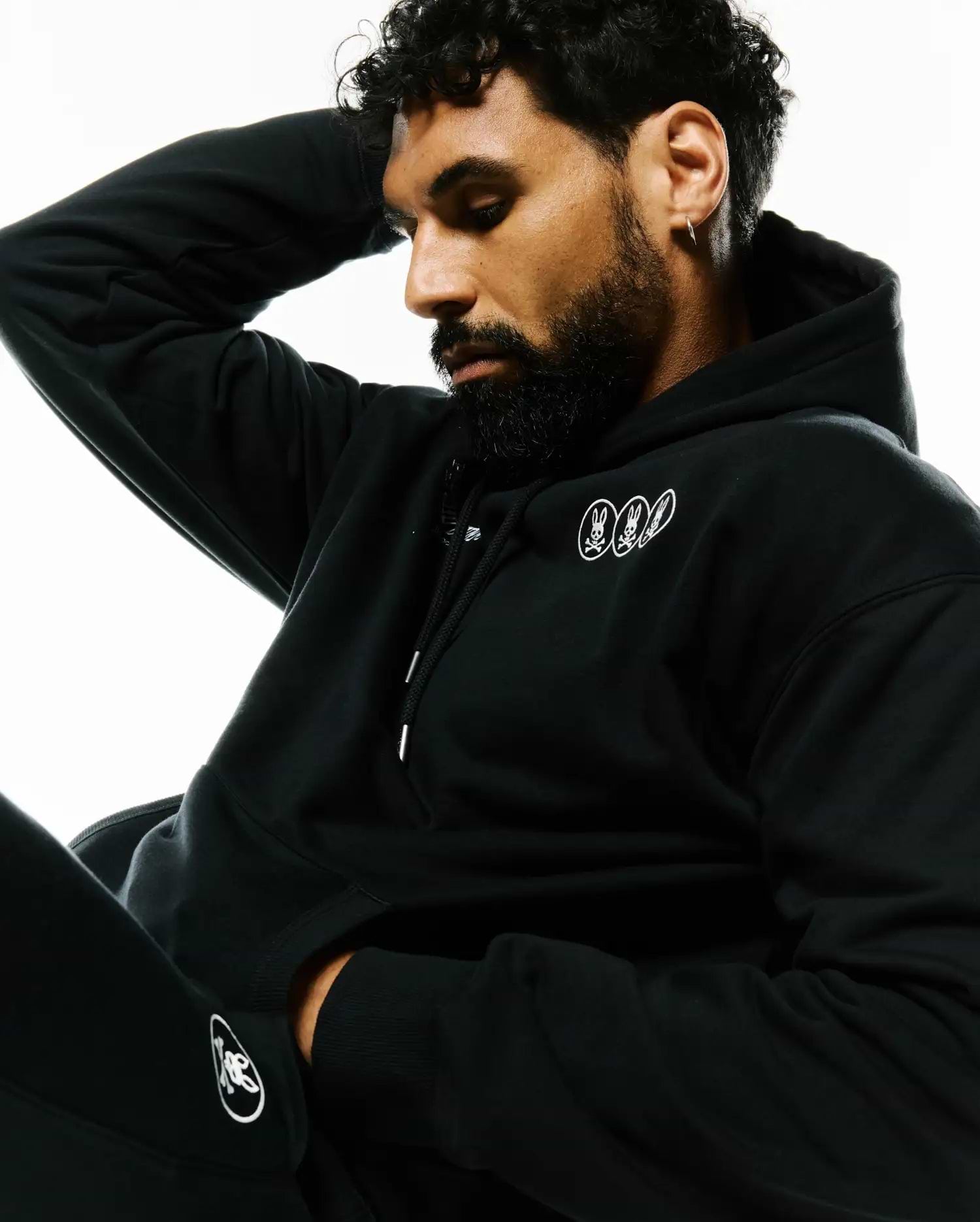 Black Mens Nathaniel Relaxed Chest Hoodie in soft French terry, featuring three small white embroidered Psycho Bunny skull logos on the left chest and a larger white logo on the left leg. (3)
