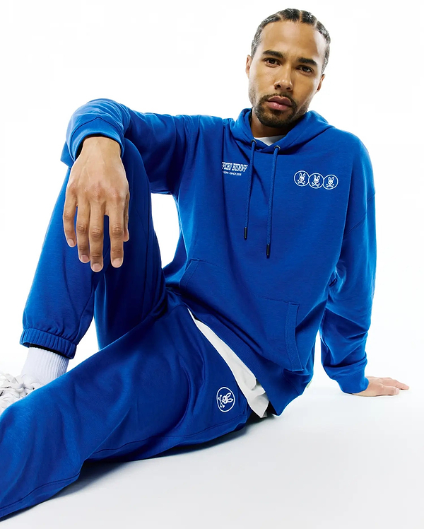 Mens Nathaniel Relaxed Chest Hoodie in royal blue soft jersey, featuring white Psycho Bunny text and three small bunny skull logos on the chest, paired with matching sweatpants with a single bunny skull logo.