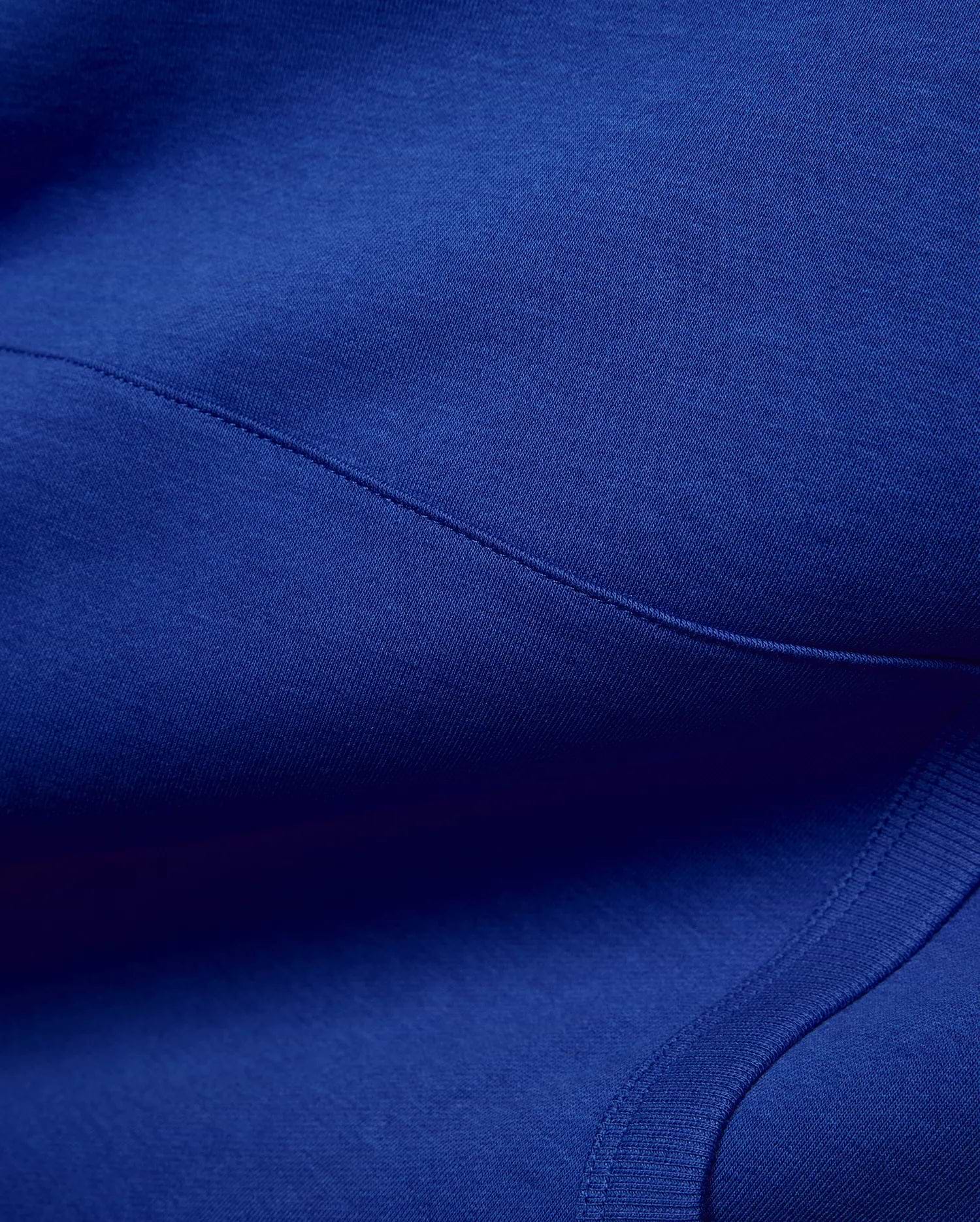 Vibrant royal blue Mens Nathaniel Relaxed Chest Hoodie, crafted from soft jersey fabric with visible seam stitching and a ribbed hem detail, embodying refined streetwear. (6)