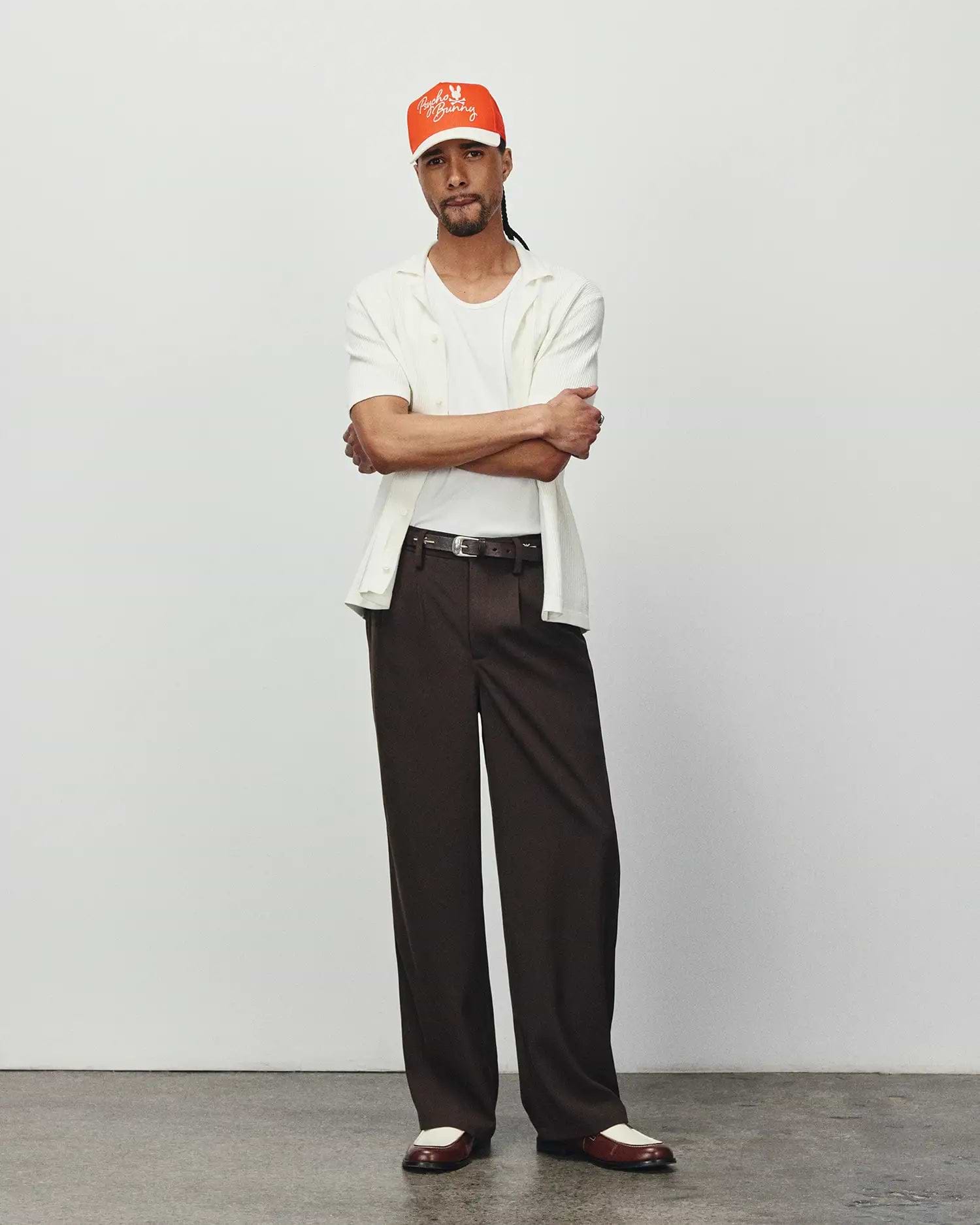 Mens Yann Knit Shirt: Relaxed fit, off-white ribbed knit short-sleeve collared shirt, layered over a white tee, with dark brown wide-leg trousers and an orange Psycho Bunny embroidered logo cap. (2)