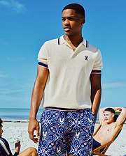 Mens Dax Knit Polo, cream pique, with navy/pink striped collar/cuffs and small navy embroidered Psycho Bunny chest logo. Navy shorts feature an all-over pink/blue skull and floral print. (1)