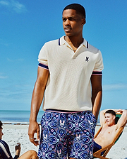 Mens Dax Knit Polo, cream pique, with navy/pink striped collar/cuffs and small navy embroidered Psycho Bunny chest logo. Navy shorts feature an all-over pink/blue skull and floral print. (1)
