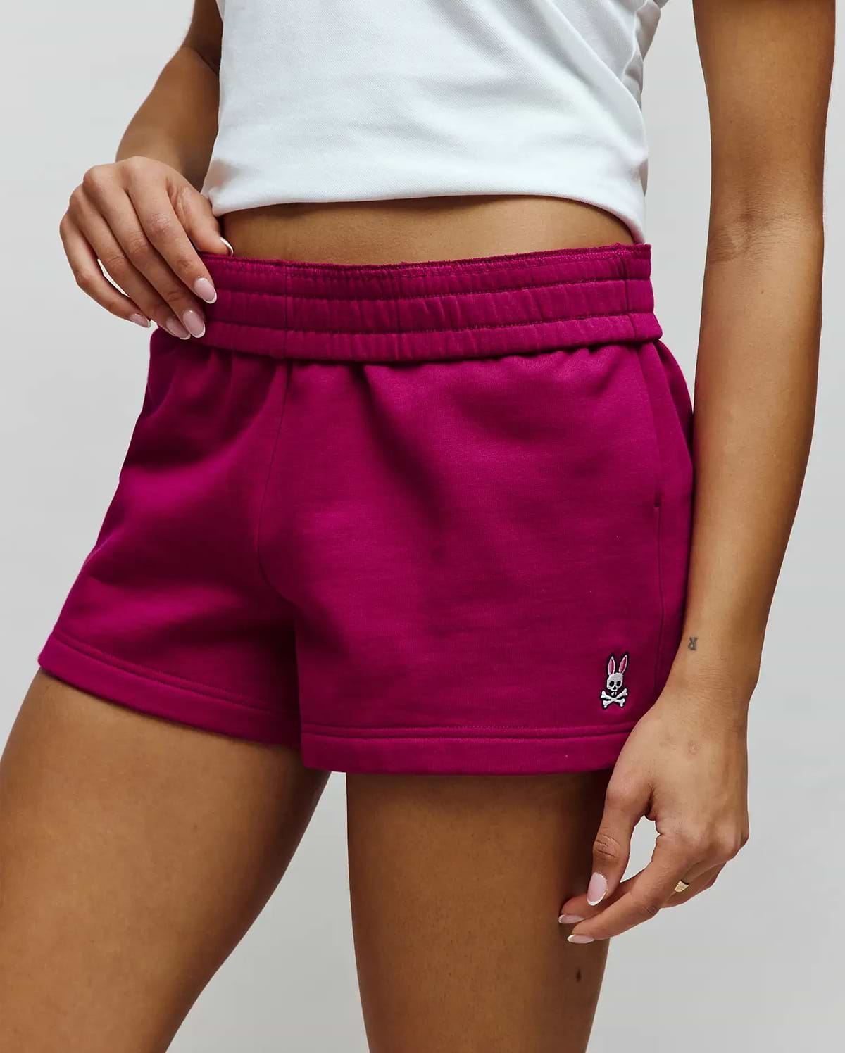 Womens Olivia Fleece Short, deep magenta, relaxed fit, soft fleece shorts with an elasticated waistband, side pockets, and a small embroidered white, black, and pink Psycho Bunny skull logo on the lower left leg. (3)