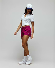 White slim-fit pique polo with small embroidered Psycho Bunny skull, paired with magenta Womens Olivia Fleece Short featuring an elastic waist and small bunny skull, and a white and navy cap with a large embroidered bunny skull. (1)