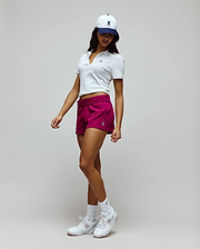 White slim-fit pique polo with small embroidered Psycho Bunny skull, paired with magenta Womens Olivia Fleece Short featuring an elastic waist and small bunny skull, and a white and navy cap with a large embroidered bunny skull. (1)