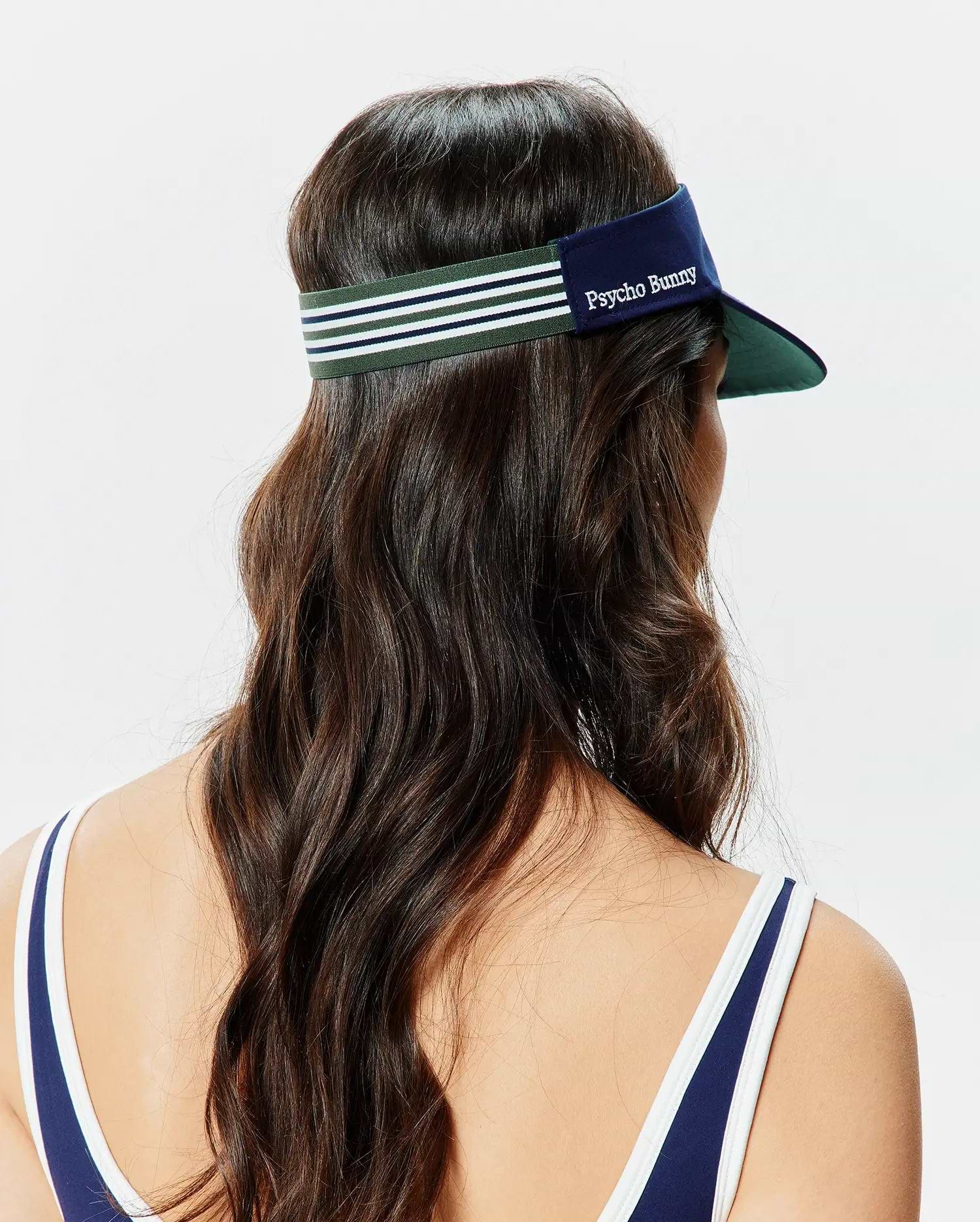 Women's Sport Visor featuring a navy blue brim with a dark green underside, complemented by a dark green elastic band with white and navy stripes. A white embroidered Psycho Bunny text logo is prominently displayed on the front. (3)