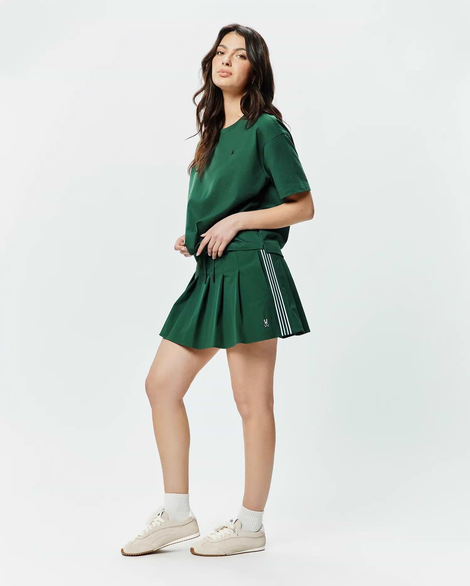 Forest green relaxed fit jersey T-shirt with a small embroidered Psycho Bunny skull on the left chest, paired with a matching Women's Cecilia Pleated Skort featuring three white side stripes and a small embroidered bunny skull. (4)