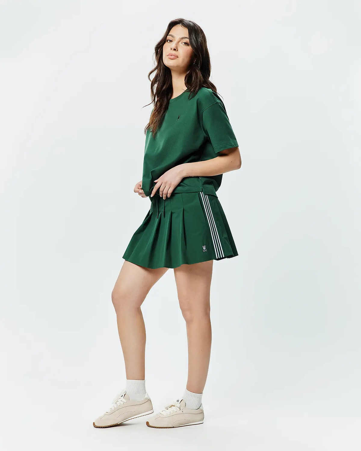 Forest green relaxed fit jersey T-shirt with a small embroidered Psycho Bunny skull on the left chest, paired with a matching Women's Cecilia Pleated Skort featuring three white side stripes and a small embroidered bunny skull. (4)