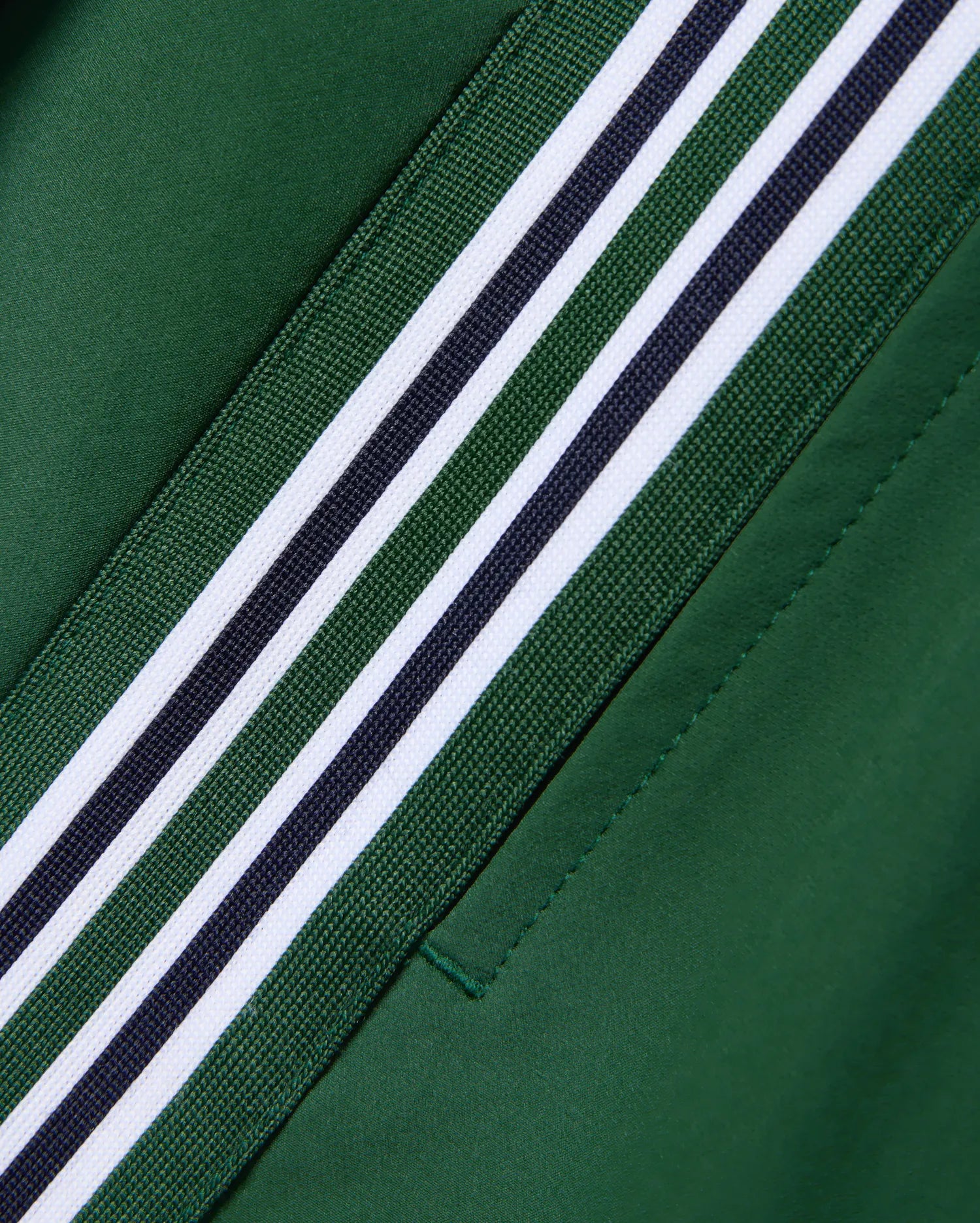 Women's Cecilia Pleated Skort in deep green, featuring a diagonal woven trim with alternating green, white, and navy stripes. Smooth fabric with visible stitching detail. (6)