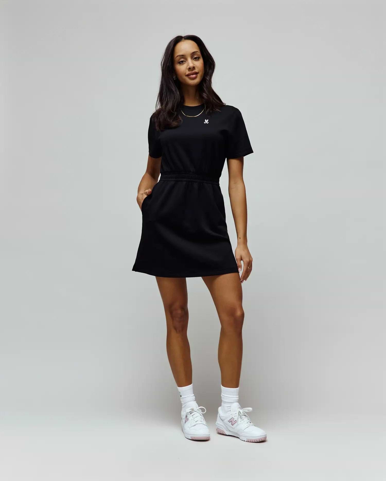 Womens Penelope Dress, a black short-sleeve jersey knit dress with a relaxed fit, crew neck, drawstring waist, side pockets, and a small embroidered white Psycho Bunny skull logo on the left chest. (1)