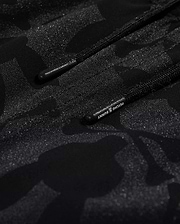 Close-up of Psycho Bunny's KIDS MALTA HYDROCHROMIC SWIM TRUNK - B0W321B2SW, showcasing a black textured fabric with a subtle camouflage pattern in shades of dark grey and black. Two parallel black cords with small text on one cord are partially visible, reminiscent of sleek swim trunks. The overall appearance is both modern and hydrochromic.