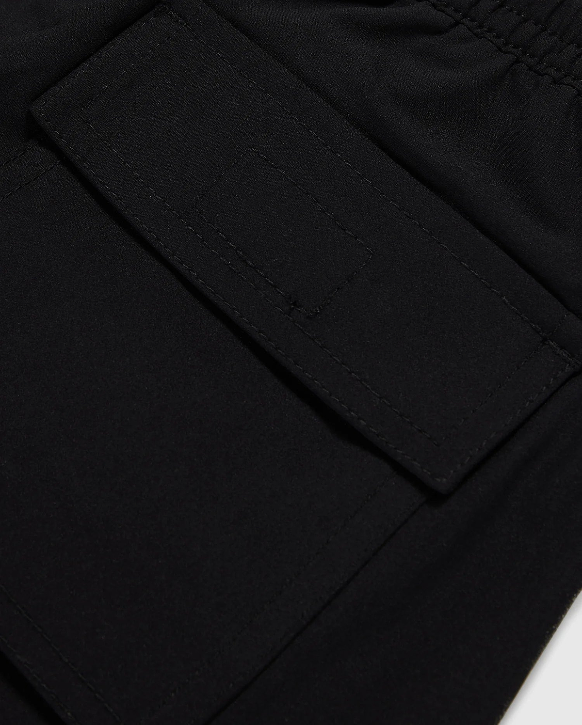Close-up image of a black fabric pocket with a flap and Velcro closure. The pocket is attached to the KIDS MALTA HYDROCHROMIC SWIM TRUNK - B0W321B2SW by Psycho Bunny, adorned with a playful bunny pattern, and the stitching around the edges is clearly visible. The fabric appears to be smooth and durable.