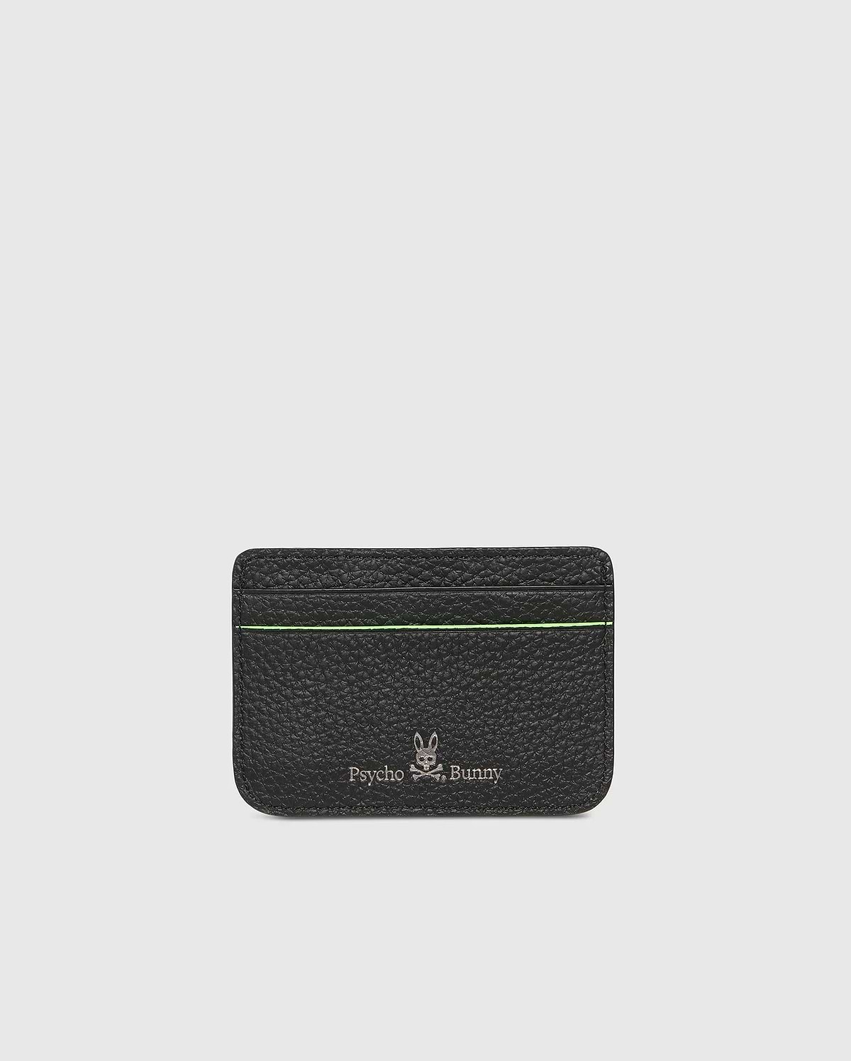 The CARD CASE - B6A409B200 by Psycho Bunny boasts a textured black leather design with a subtle green stripe near the top. Embossed at the bottom are the silver Psycho Bunny logo and name, set against a plain, light gray background for added elegance.