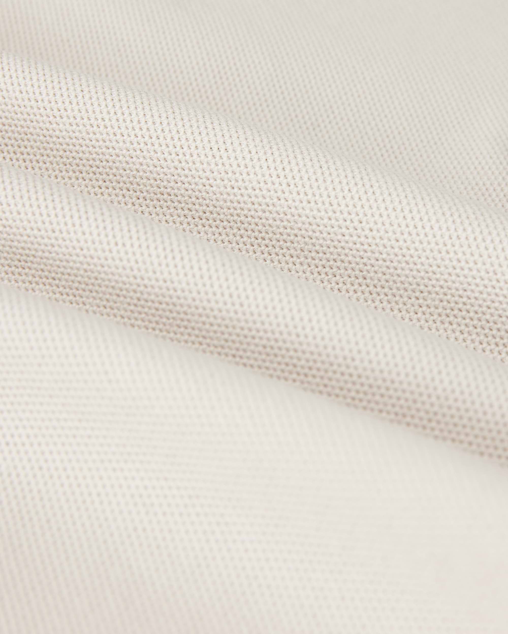 A close-up shows the Psycho Bunny MENS CLASSIC PIQUE POLO SHIRT - B6K001B200, with a textured weave pattern. The soft white fabric resembles fine Pima cotton, with subtle shadowing in the folds that exude timeless men's fashion.