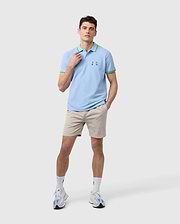 A person dressed in a light blue polo shirt with green accents, paired with the MENS WILLIS STRETCH TENCEL SHORT - B6R239Y1WB by Psycho Bunny, along with white socks and sneakers, stands against a plain background. The shirt is adorned with a small green logo on the chest.