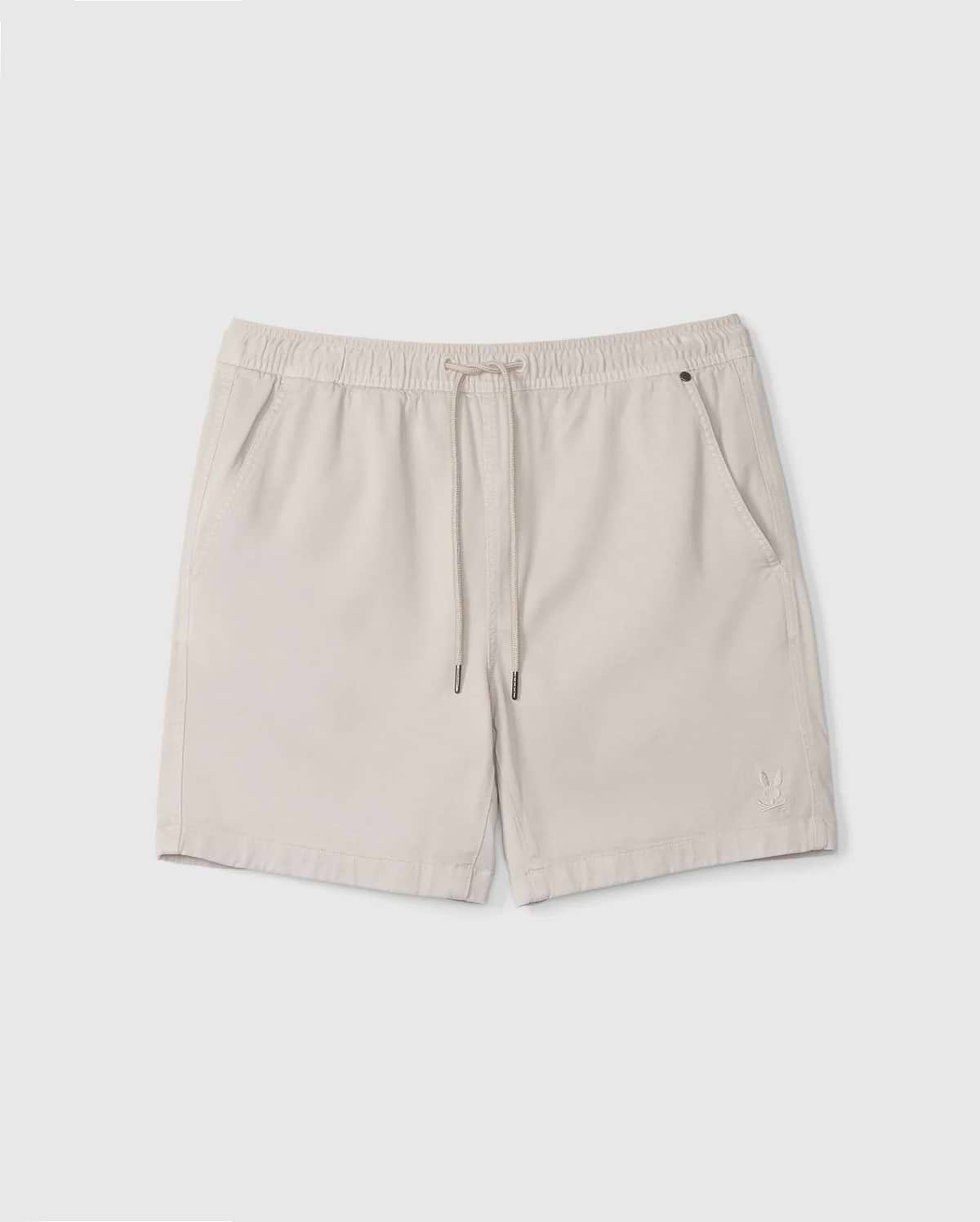 A pair of beige Men's Willis Stretch TENCEL™ shorts from Psycho Bunny, featuring an elastic waistband with a drawstring, two front pockets, and a small embroidered logo on the lower left. The lightweight fabric makes them ideal for casual wear.
