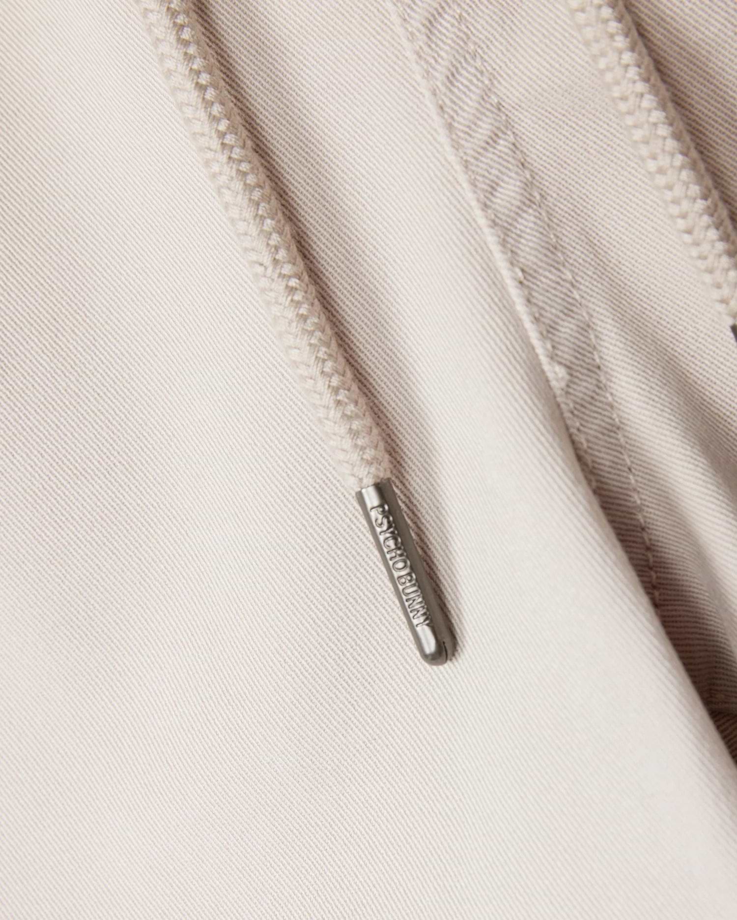 Close-up of a beige hoodie showcasing a metal zipper pull engraved with "ARMANI EXCHANGE." The visible fabric texture and detailed stitching around the zipper make it an ideal pairing with the Psycho Bunny MENS WILLIS STRETCH TENCEL SHORTS or elasticated waist trousers.