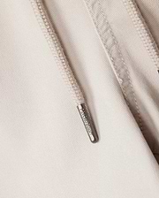 Close-up of a beige hoodie showcasing a metal zipper pull engraved with "ARMANI EXCHANGE." The visible fabric texture and detailed stitching around the zipper make it an ideal pairing with the Psycho Bunny MENS WILLIS STRETCH TENCEL SHORTS or elasticated waist trousers.