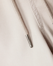 Close-up of a beige hoodie showcasing a metal zipper pull engraved with "ARMANI EXCHANGE." The visible fabric texture and detailed stitching around the zipper make it an ideal pairing with the Psycho Bunny MENS WILLIS STRETCH TENCEL SHORTS or elasticated waist trousers.