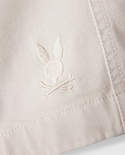 A close-up of the white fabric on the Psycho Bunny MENS WILLIS STRETCH TENCEL SHORT - B6R239Y1WB reveals an embroidered logo featuring a rabbit head and crossbones. The stitching seamlessly blends with the fabric's hue, while the texture accentuates the embroidery's details, providing an eco-friendly twist to stylish comfort.