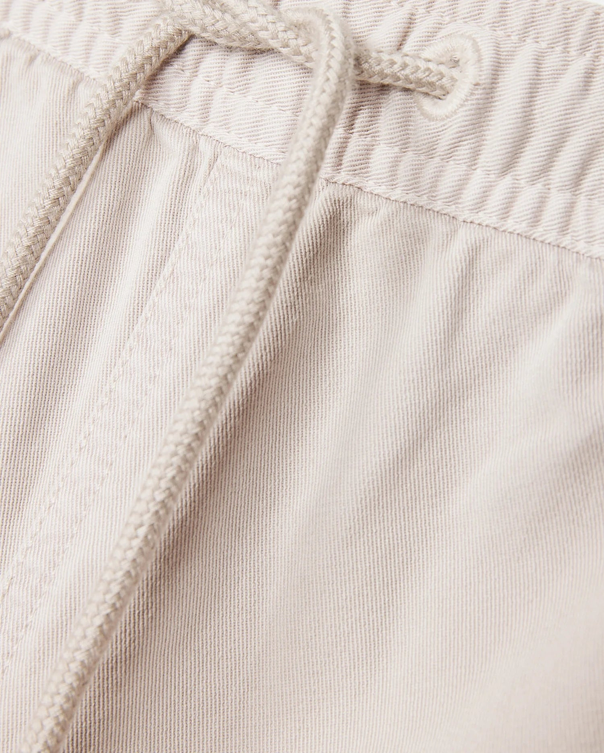 Close-up of the light beige Psycho Bunny MENS WILLIS STRETCH TENCEL SHORT - B6R239Y1WB, featuring an elasticated waistband with a drawstring. The fabric texture and stitching details are clearly visible, exemplifying the perfect combination of style and comfort.