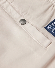 Close-up of the beige fabric from the Men's Willis Stretch TENCEL Shorts (B6R239Y1WB), showcasing a silver button embossed with "Psycho Bunny." A blue label featuring a white logo and text is sewn next to the pocket, completing these stylish eco-friendly men's shorts.