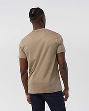 A person with cornrowed hair is seen from the back, wearing the Psycho Bunny MENS CLASSIC CREW NECK TEE - B6U014CRPC made of 100% Pima cotton and dark jeans. The light beige short-sleeve shirt serves as the basis for any man's wardrobe, standing out against the plain white background and highlighting the individual's casual attire and hairstyle.