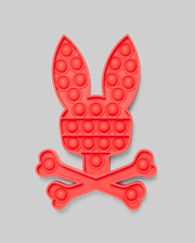 The PSYCHO BUNNY POP IT - B0A376E200 by Psycho Bunny features a red bunny head with long ears above crossed bones, resembling a fun skull-and-crossbones. Made from high-quality silicone for stress relief, set against a light gray background.