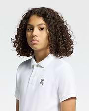 A person with curly hair wears a Psycho Bunny Kids Classic Pique Polo Shirt (B0K001CRPC), featuring a small embroidered logo on the chest. The plain, light background highlights this timeless choice, ideal for back-to-school outfits.