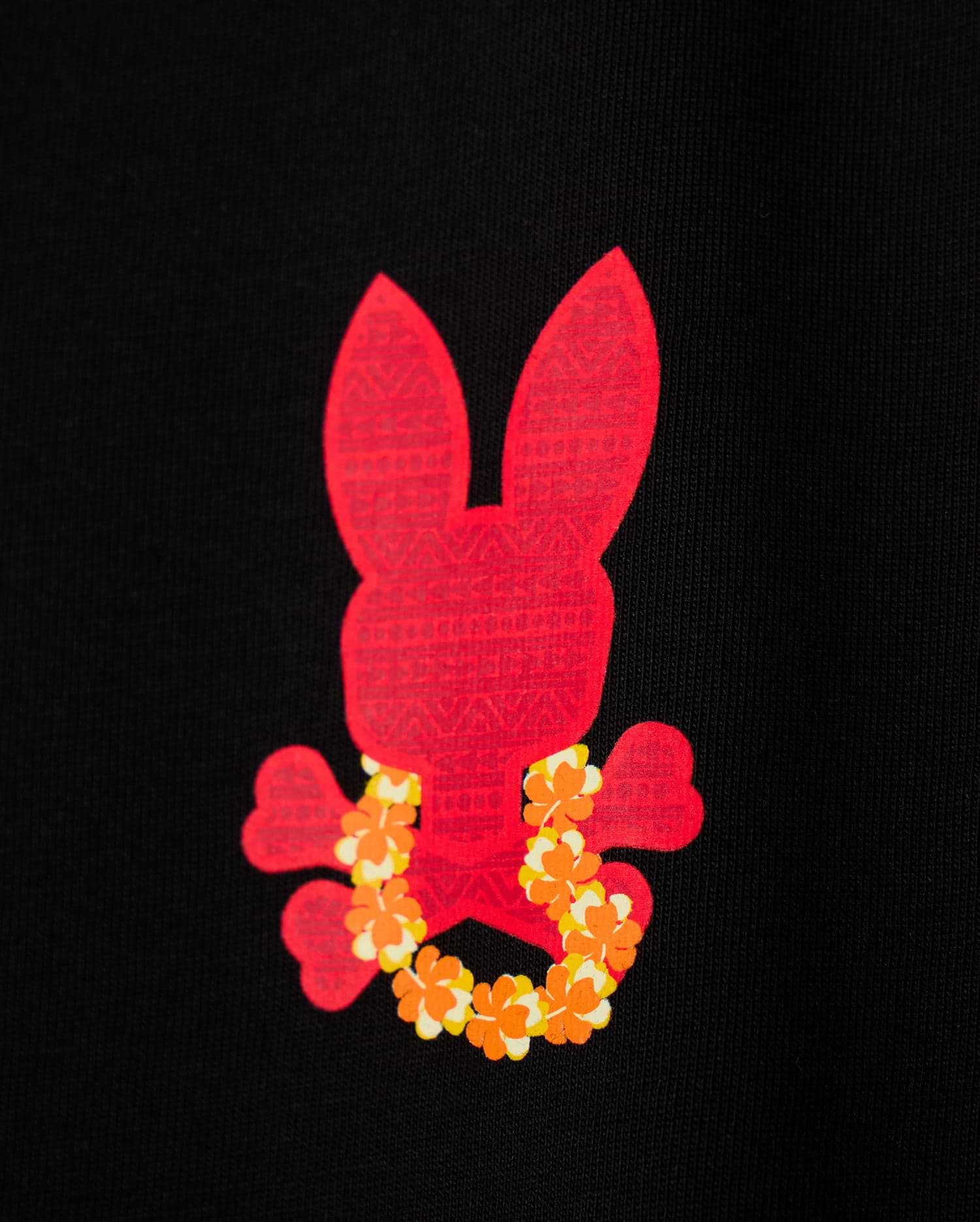 The KIDS HAWAII CITY TEE by Psycho Bunny features a red bunny skull and crossbones design surrounded by yellow and orange flowers, set against a black backdrop inspired by Hawaii's vibrant volcanic flora.