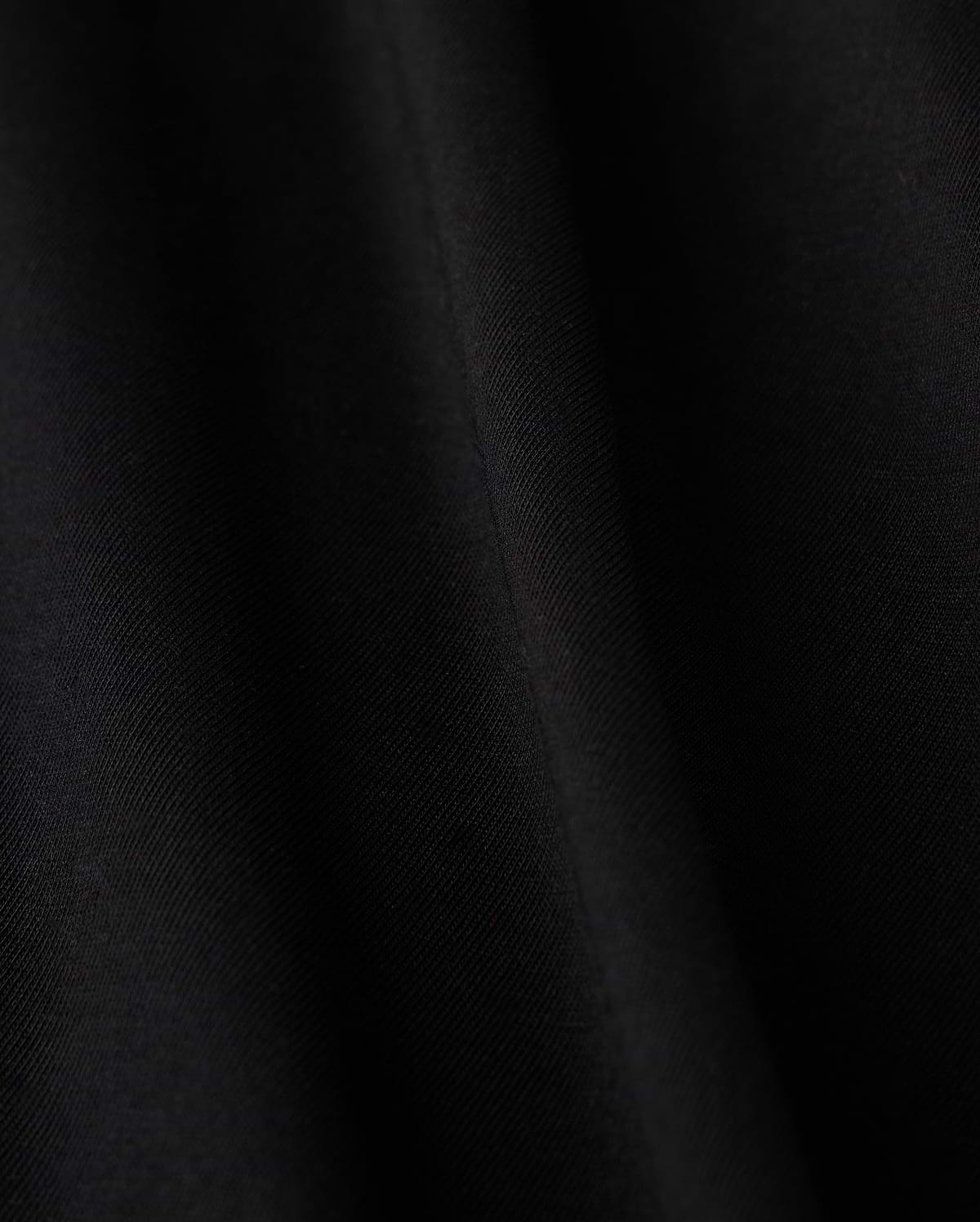 Close-up of a smooth black fabric crafted from luxurious Pima cotton on Psycho Bunny's KIDS HAWAII CITY TEE - B0U169Y1PC, featuring subtle diagonal lines and a soft sheen, evoking the sleek elegance reminiscent of volcanic island landscapes.