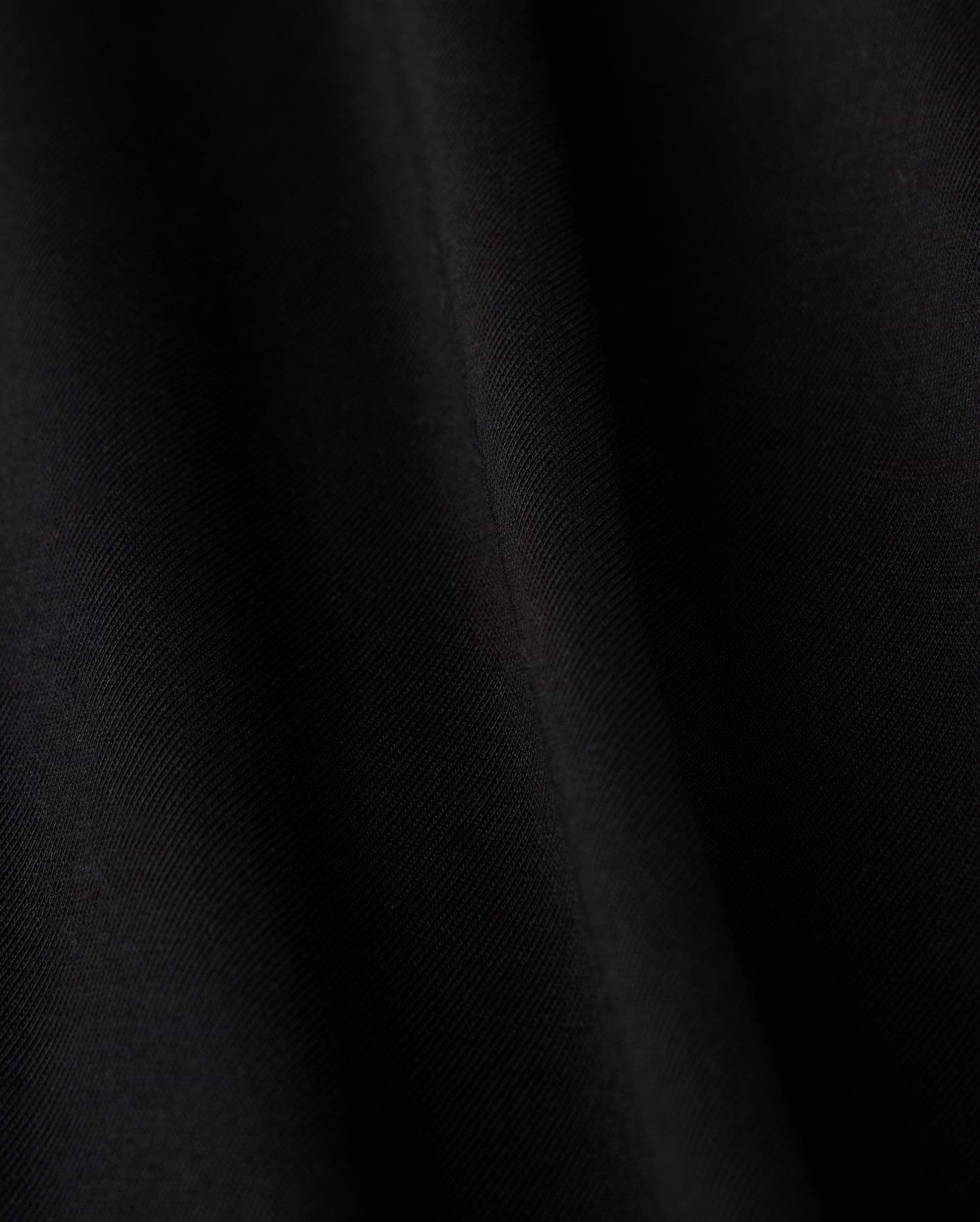 Close-up of a smooth black fabric crafted from luxurious Pima cotton on Psycho Bunny's KIDS HAWAII CITY TEE - B0U169Y1PC, featuring subtle diagonal lines and a soft sheen, evoking the sleek elegance reminiscent of volcanic island landscapes.