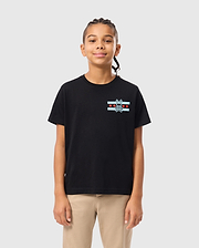 A young person with braided hair is wearing the KIDS CHICAGO CITY TEE from Psycho Bunny, a black Pima cotton jersey featuring red and white stripes and a small emblem, paired with beige pants, standing against a plain light gray background.