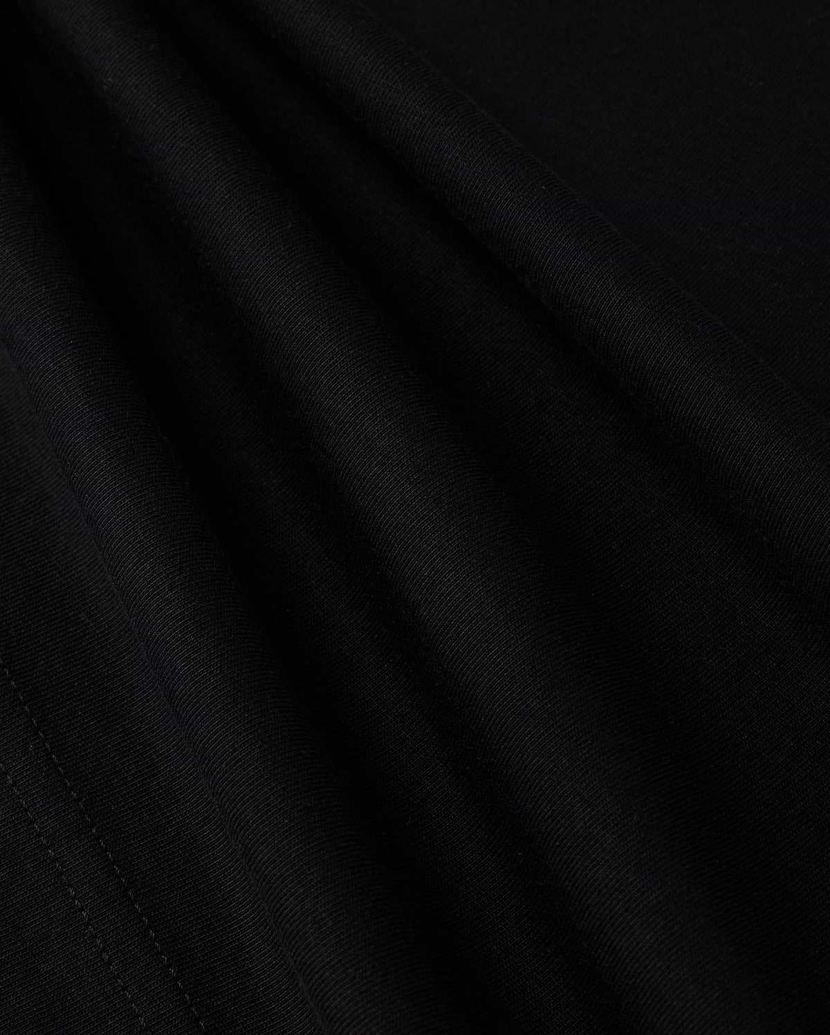 A close-up view of the smooth, dark fabric of the KIDS LOS ANGELES CITY TEE - B0U861A2PC by Psycho Bunny shows a fine, consistent weave. The folds create subtle shadows and highlights, accentuating the texture and soft appearance of this luxurious Peruvian Pima cotton material, suggesting it is well-crafted and of high quality.