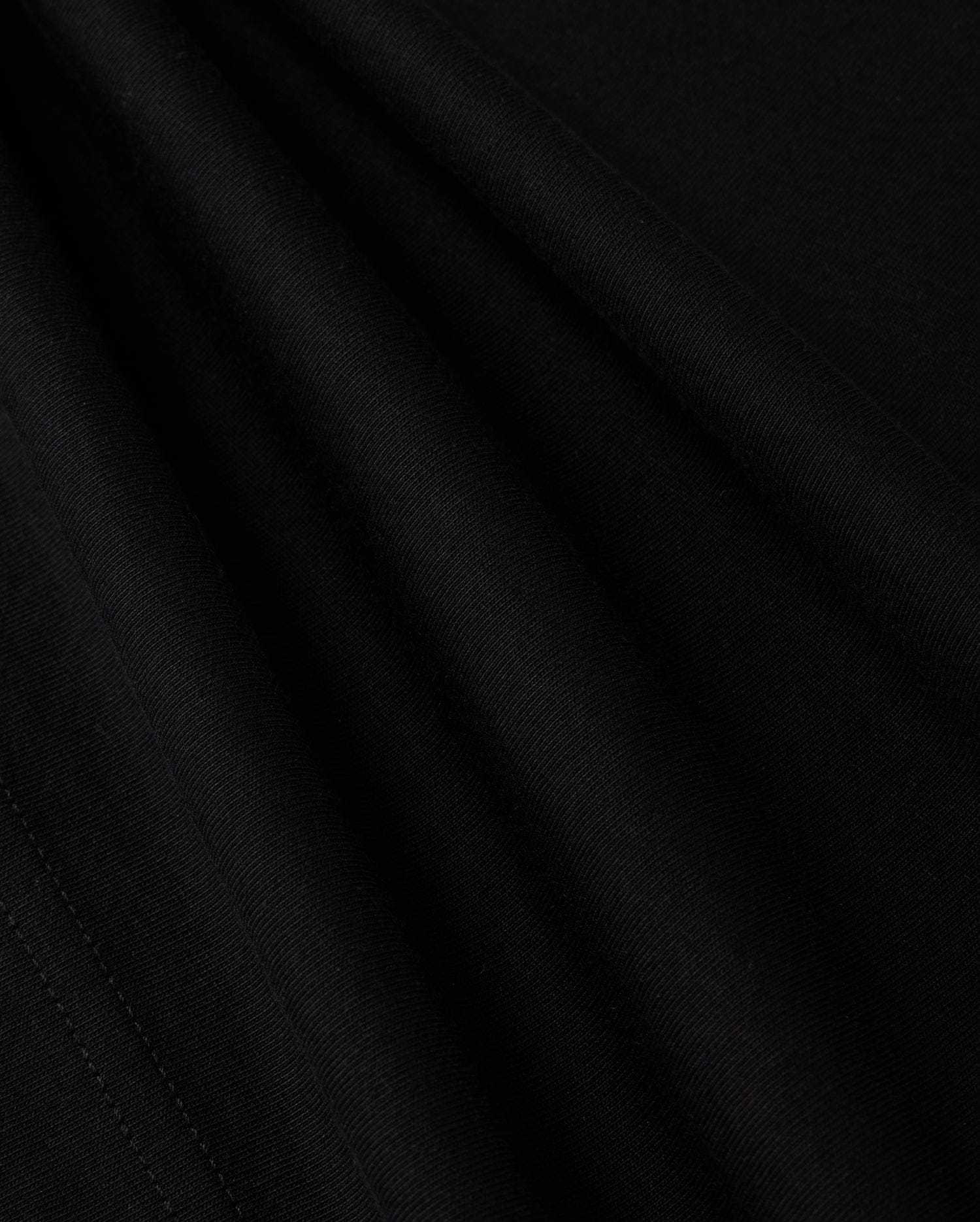 A close-up view of the smooth, dark fabric of the KIDS LOS ANGELES CITY TEE - B0U861A2PC by Psycho Bunny shows a fine, consistent weave. The folds create subtle shadows and highlights, accentuating the texture and soft appearance of this luxurious Peruvian Pima cotton material, suggesting it is well-crafted and of high quality.