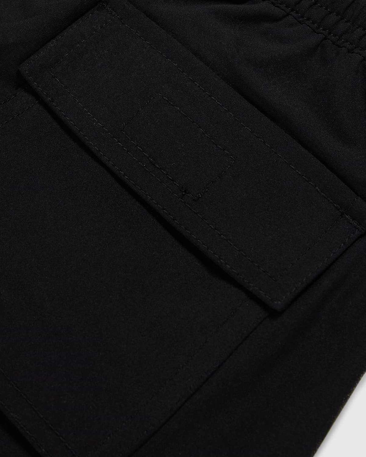 Close-up of a black polyester mechanical stretch fabric with a detailed view of a stitched rectangular patch pocket on Psycho Bunny's KIDS MALTA HYDROCHROMIC SWIM TRUNK - B0W321B2SW.