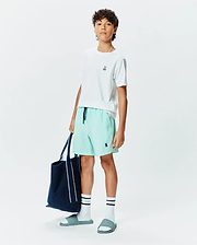White classic fit jersey t-shirt with small embroidered Psycho Bunny logo, Kids Samos Hydrochromic Printed Swim Trunk in mint green with navy drawstring and embroidered logo, white crew socks with black stripes and Psycho text, and teal slides with embossed logo.