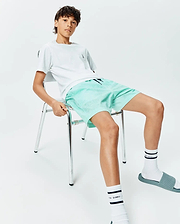 White t-shirt with small embroidered Psycho Bunny skull logo on chest, paired with Kids Samos Hydrochromic Printed Swim Trunk in mint green featuring a subtle all-over bunny skull pattern, and white Psycho Bunny socks.